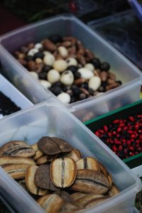 Variety of seeds and beans displayed in plastic containers for sale at a market.